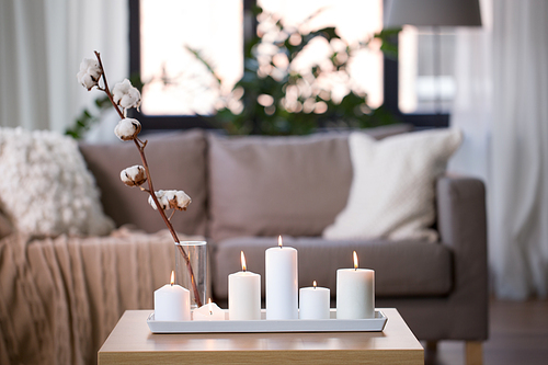 decoration, hygge and cosiness concept - burning white candles and cotton flower branch on table at cozy home