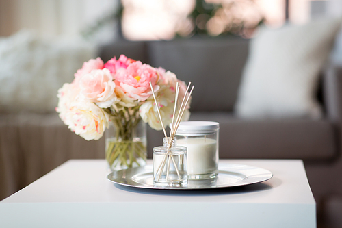 decoration, hygge and cosiness concept - aroma reed diffuser, candle and flower bunch on wooden table