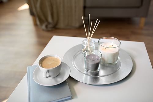 hygge and aromatherapy concept - coffee, candles, book and aroma reed diffuser on table at home