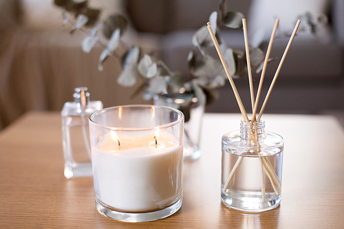 decoration, hygge and aromatherapy concept - aroma reed diffuser, burning candle and perfume on table at home