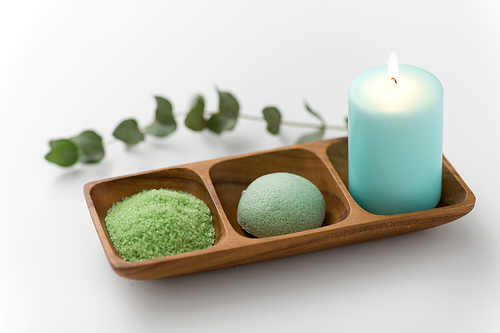 beauty, spa and wellness concept - green bath salt, konjac sponge and candle on wooden tray with eucalyptus cinerea