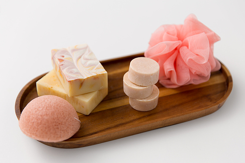 beauty, spa and wellness concept - close up of crafted soap bars, konjac sponge and wisp on wooden tray