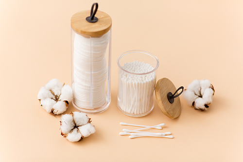 beauty and hygiene concept - close up of cotton pads and swabs in holders on beige background