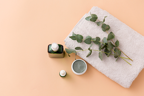 beauty, spa and wellness concept - serum, clay mask, oil and eucalyptus cinerea on bath towel
