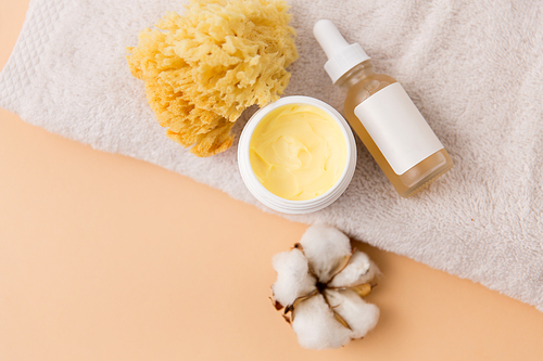 beauty, spa and wellness concept - close up of body butter, natural sponge and essential oil on bath towel