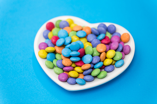 sweets, confectionery and valentine's day concept - candy drops on heart shaped plate over blue background