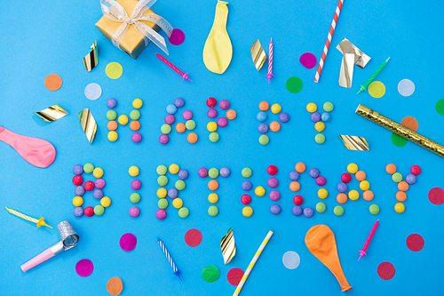 food, confectionery and sweets concept - happy birthday lettering made of candy drops and party props on blue background