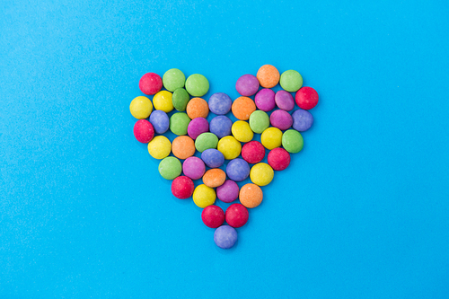 sweets, confectionery and valentine's day concept - bright multicolored candy drops in shape of heart on blue background