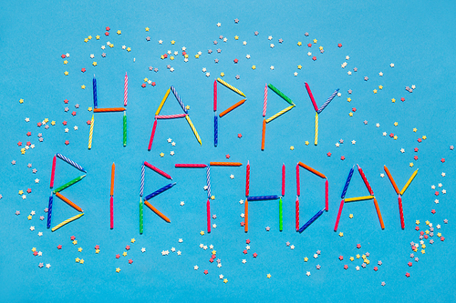 holiday, celebration and party concept - words happy birthday made of colorful candles and star shaped sugar sprinkles on blue background