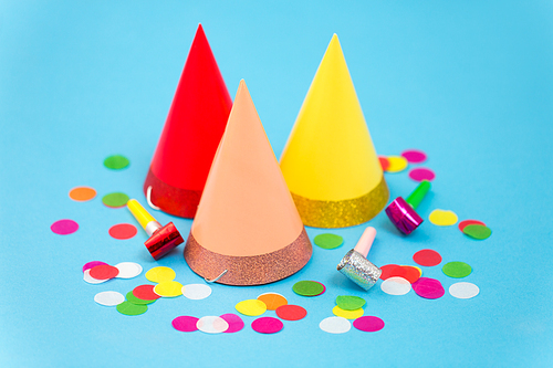 celebration and decoration concept - three birthday party caps, horns and colorful confetti on blue background