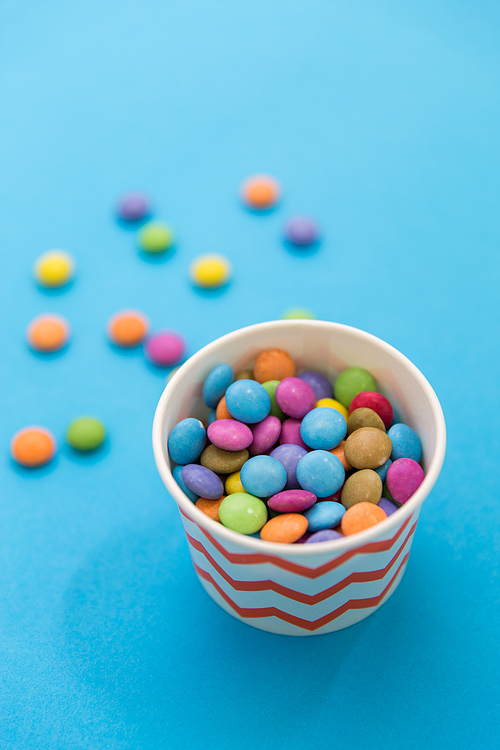 food, confectionery and sweets concept - candy drops in paper cup on blue background
