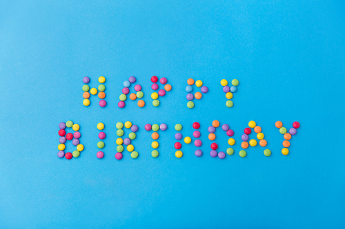 food, confectionery and sweets concept - happy birthday lettering made of candy drops on blue background