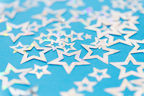 party, celebration and decoration concept - holographic star shaped confetti on blue background
