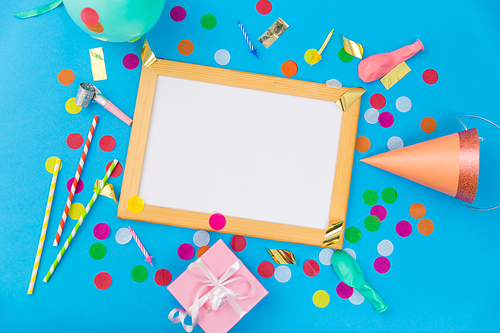 celebration and decoration concept - white board in frame, pink birthday gift, party props, balloons and colorful confetti on blue background