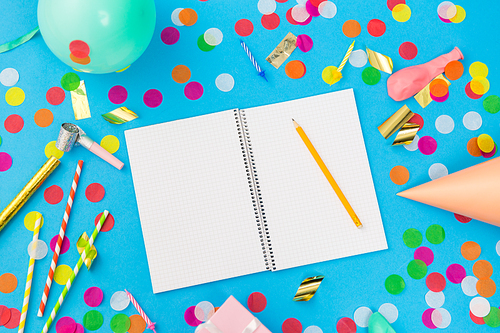 celebration and decoration concept - notebook with pencil and birthday party props on blue background