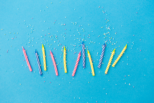 holiday, celebration and party concept - birthday candles with sprinkles on blue background