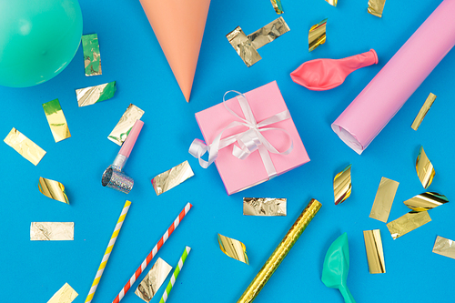 celebration and decoration concept - pink birthday gift, party props, balloons and colorful confetti on blue background