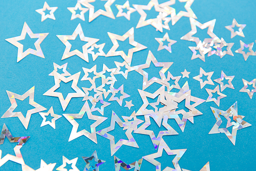 party, celebration and decoration concept - holographic star shaped confetti on blue background