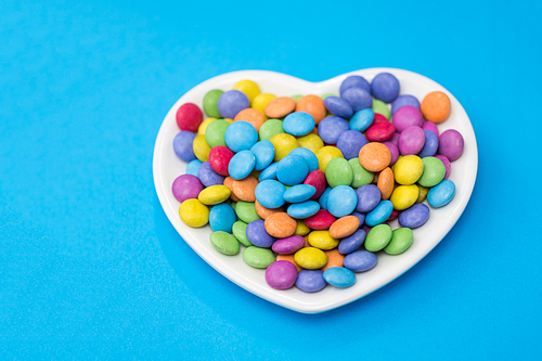 sweets, confectionery and valentine's day concept - candy drops on heart shaped plate over blue background