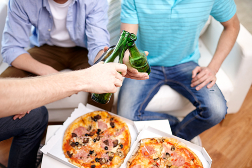 friendship, alcohol, people, celebration and holidays concept - close up of male hands clinking beer bottles and eating pizza at home
