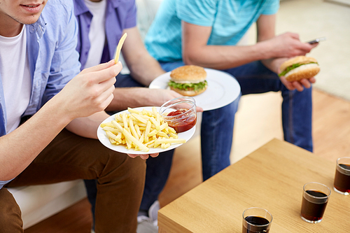 fast food, unhealthy eating, people and junk-food - close up of happy friends eating french fries and hamburgers at home