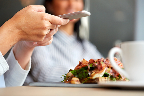 food, dinner, eating, technology and people concept - woman with smartphone and prosciutto ham salad on stone plate at restaurant