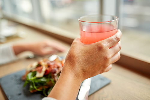 food, drink, eating and people concept - hand with glass of juice and salad at restaurant