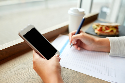 business, people, technology and lifestyle concept - woman with smartphone and paper form writing at cafe