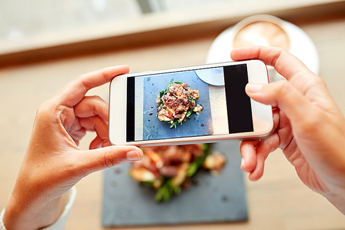 food, culinary, technology and people concept - woman hands with smartphone photographing prosciutto ham salad on stone plate at restaurant