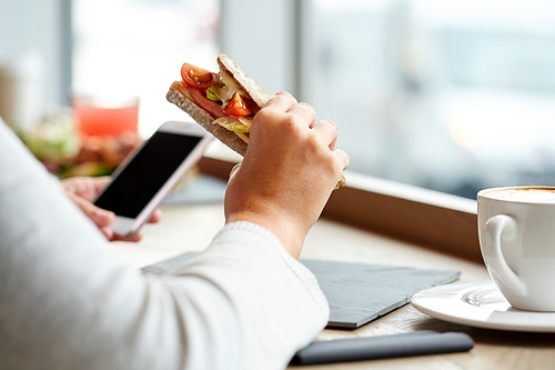 food, dinner, technology and people concept - woman with smartphone eating salmon panini sandwich with tomatoes and cheese at restaurant