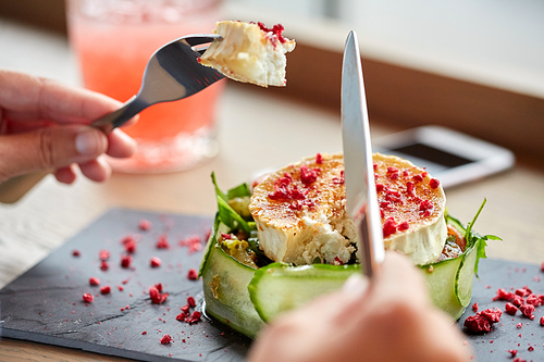 food, culinary, haute cuisine and people concept - woman eating goat cheese salad with fork and knife at restaurant or cafe