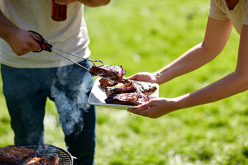 food, people, eating and cooking concept - man with tongs putting barbecue meat on plate at summer party