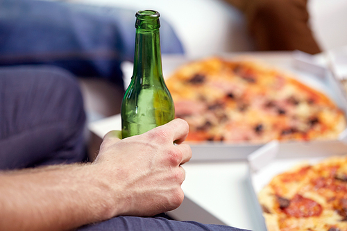 alcohol and people concept - man with beer bottle and pizza at home