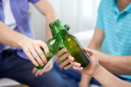 people, celebration and alcohol concept - close up of friends clinking beer bottles at home