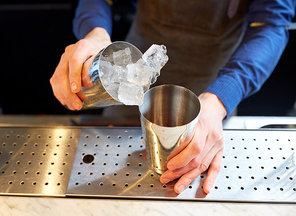 alcohol drinks, people and luxury concept - bartender adding ice into shaker preparing cocktail at bar
