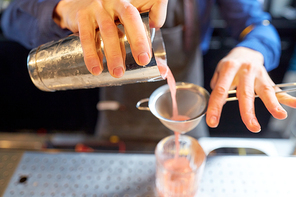 alcohol drinks, people and luxury concept - barman pouring cocktail from shaker through strainer into glass at bar