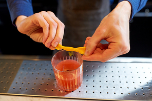 alcohol drinks, people and luxury concept - bartender with glass and orange peel preparing cocktail at bar