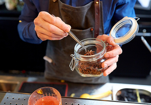 alcohol drinks, people and luxury concept - bartender with tongs taking anise from jar and preparing cocktail at bar