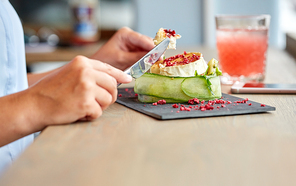 food, culinary, haute cuisine and people concept - woman eating goat cheese salad with vegetables and dried raspberries using fork and knife at restaurant or cafe