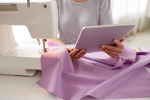 people, needlework, technology and tailoring concept - tailor woman with sewing machine, tablet pc and fabric