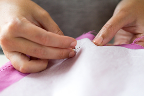 people, needlework and tailoring concept - tailor woman with pins stitching paper pattern to fabric at sewing studio