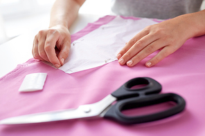 people, needlework and tailoring concept - tailor woman with pins stitching paper pattern to fabric at sewing studio