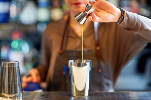 alcohol drinks, people and luxury concept - woman bartender with jigger pouring syrup into shaker and preparing cocktail at bar counter