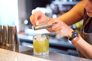 alcohol drinks, people and luxury concept - close up of woman bartender with glass and grater grates white chocolate preparing cocktail at bar
