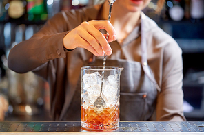 alcohol drinks, people and luxury concept - woman bartender with stirrer and glass preparing cocktail at bar counter