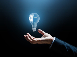 business, idea, inspiration and people concept - close up of businessman hand with light bulb over dark background