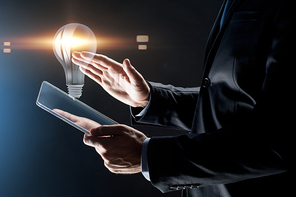 business, people and future technology concept - close up of businessman hands with transparent tablet pc computer and lightbulb projection over black background