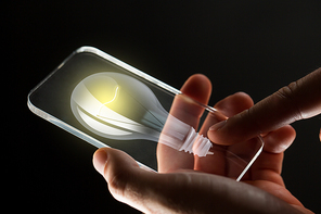 business, solution, idea, people and future technology concept - close up of hands with lightbulb on transparent smartphone screen over black background