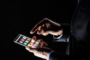 business, multimedia, people and modern technology concept - close up of businessman hands with transparent smartphone with menu icons on screen over black background