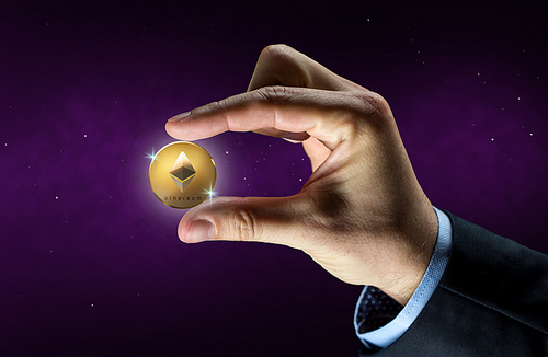 cryptocurrency, financial technology and business concept - businessman hand with golden ethereum coin over ultra violet space background